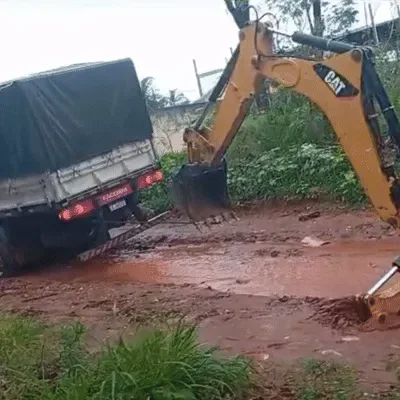 Carreta atola em vala durante chuva e precisa de retroescavadeira para socorrer