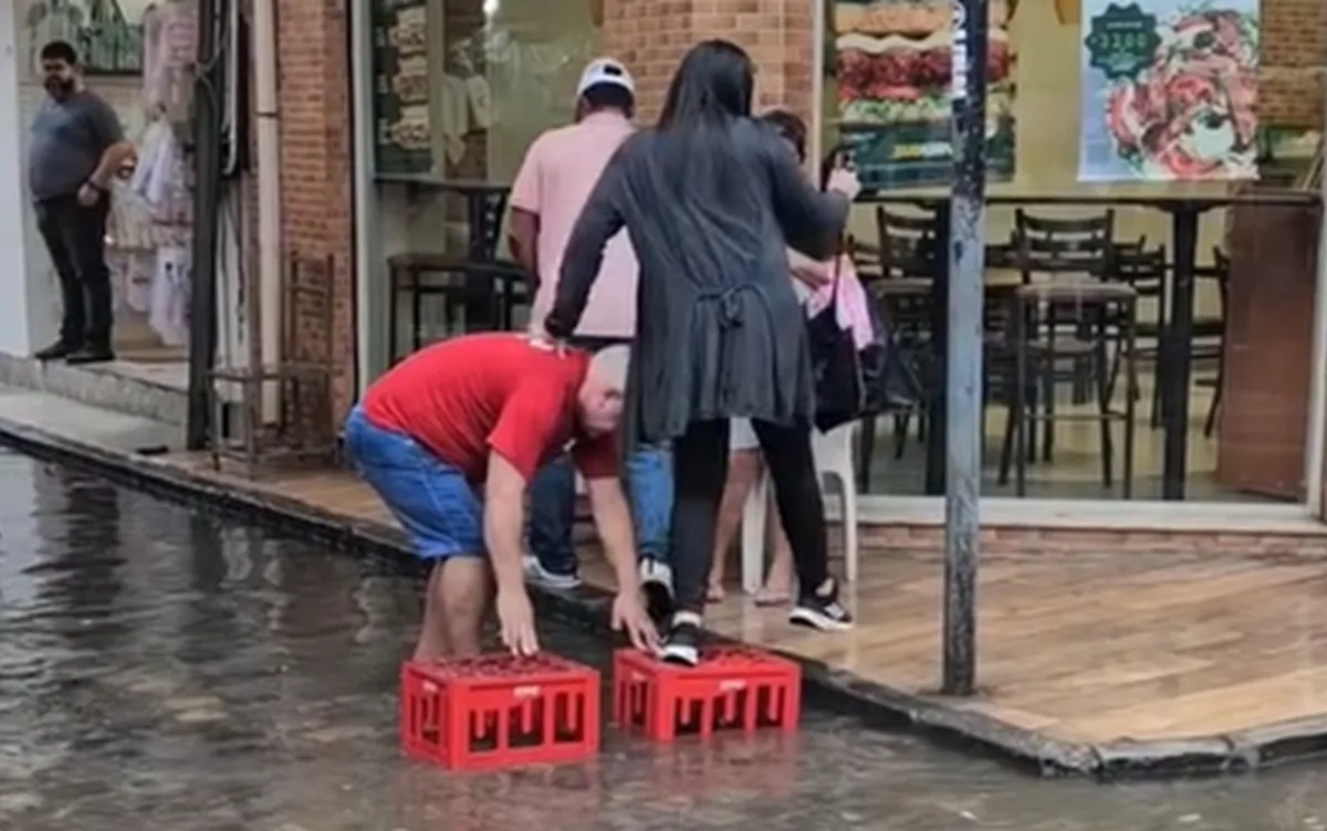 Homem improvisa ponte e ajuda pessoas a atravessar rua alagada no Centro do Recife; VÍDEO